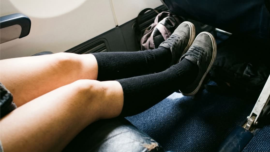 Airplane seat with dark knee-high socks and sneakers.